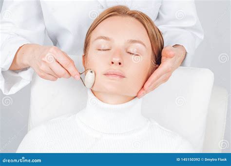 Beautiful Woman Having Face Treatment Cosmetologist Massaging Chin With Jade Rollers Stock