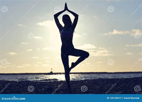 Silhouette Young Woman Practicing Yoga On The Beach At Sunset Stock