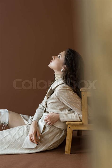 Side View Of Beautiful And Trendy Woman Sitting On Floor Looking Up
