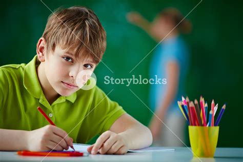 Portrait Of Cute Schoolboy Drawing With Colorful Pencils And Looking At