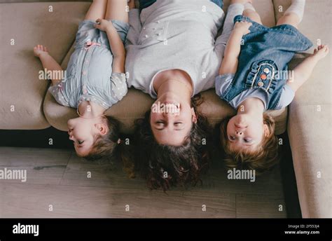 A Young Mother And Two Young Daughters Are Lying On The Sofa Upside