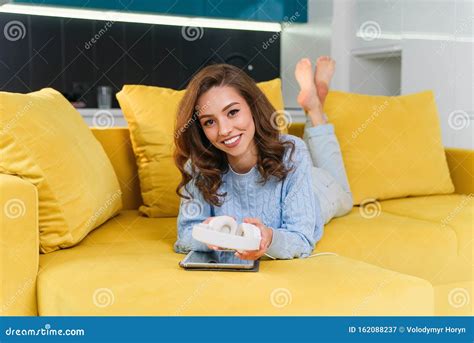 Satisfied Happy Girl Using Tablet While Lying On Comfortable Yellow Sofa And Enjoying Pleasant