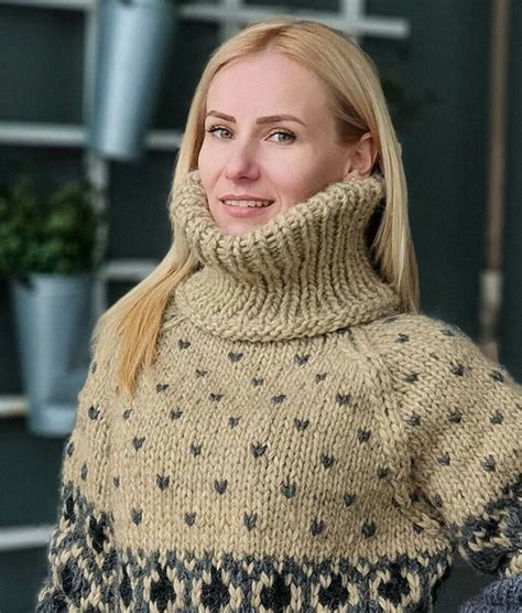 A Woman With Blonde Hair Wearing A Tan And Black Knitted Turtle Neck