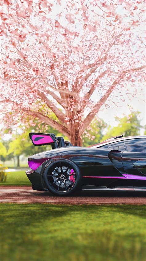 A Black Sports Car Parked In Front Of A Tree With Pink Flowers On The Branches