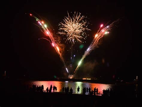 fireworks are lit up in the night sky over water and people standing on the beach