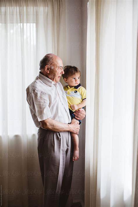 grandfather with his grandson looking outside of a window by stocksy contributor nasos