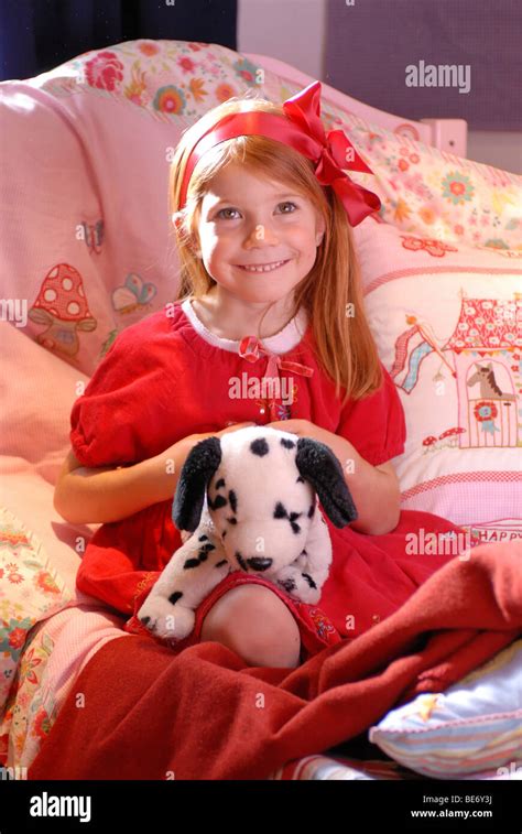 Little Girl Wearing A Romantic Red Dress Sitting On Her Bed And Playing