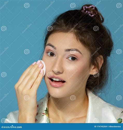cheerful attractive teen girl clean her face with cotton disk isolated over blue background