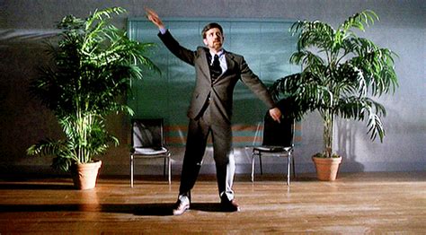 A Man In A Suit And Tie Standing On A Wooden Floor Next To Potted Plants