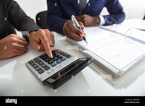 Close Up Of Two Accountants Calculating Tax Invoice Using Calculator On