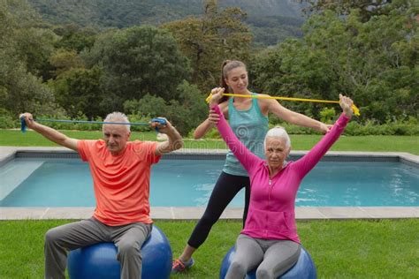 Female Trainer Assisting Active Senior Couple To Exercise With