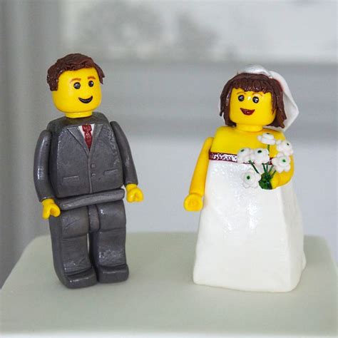 A Lego Bride And Groom Standing Next To Each Other On Top Of A White Cake