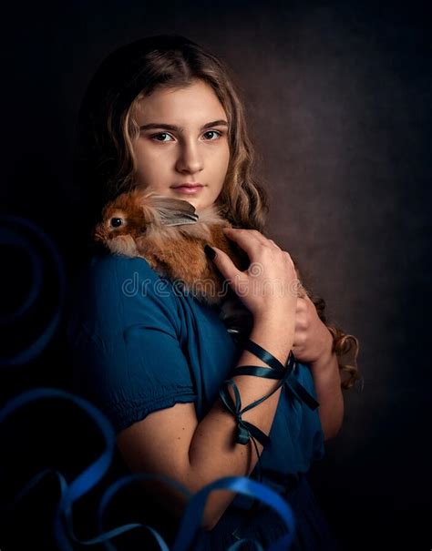 A Brunette Girl With Long Curly Hair In A Blue Dress Holds A Red Rabbit