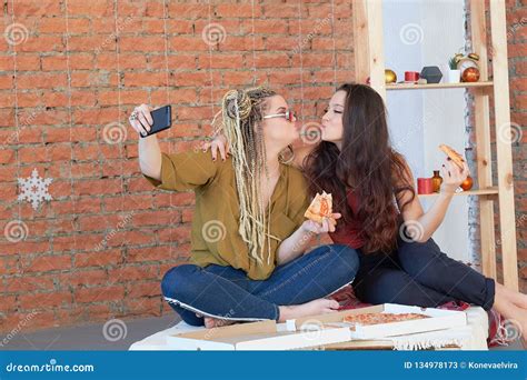 two girls eat pizza in the room on the bed make selfie on your smartphone junk food stock