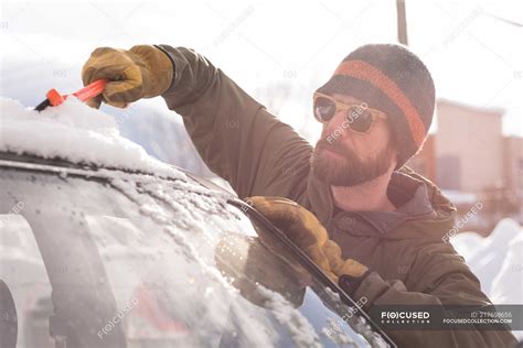 Man Cleaning Snow From Car Windshield During Winter — 20s Expertise