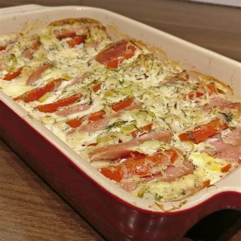 A Casserole Dish With Ham Tomatoes And Cheese In It On A Wooden Table