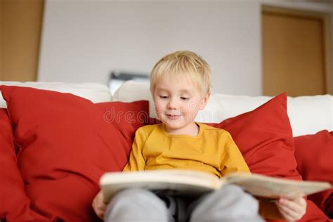 Little Boy Is Sitting At Home On The Couch And Reading A Book Learning