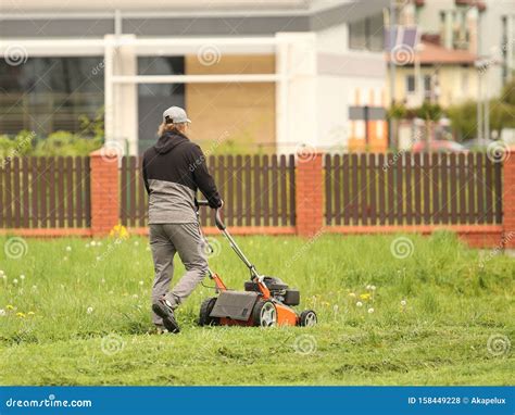 Worker Using A Manual Lawn Mower Mows Grass On Near The House