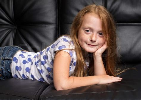 little redhead girl with freckles resting on black sofa stock image colourbox