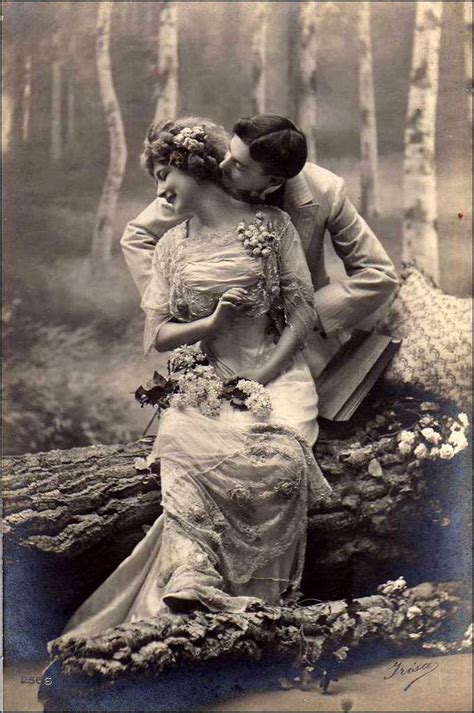 an old fashion photo of two women sitting on a tree trunk in the woods kissing