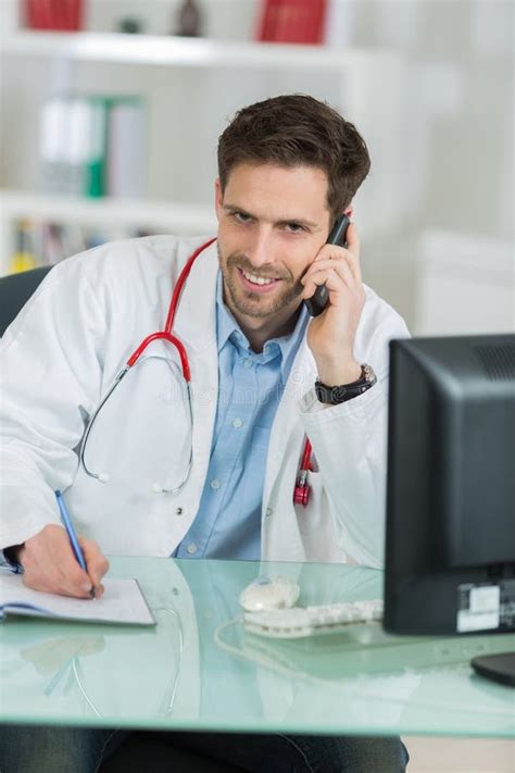 Young Male Doctor Sitting At Desk And Phoning Stock Photo Image Of