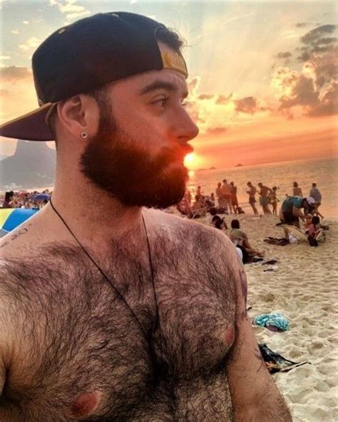 A Man With A Beard And No Shirt On At The Beach In Front Of People