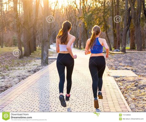 Two Young Women Run Along The Path In The Park Back View Stock Photo