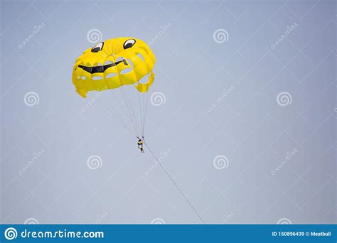 Woman Flying On A Yellow Parachute With Smiling Face On It Stock Image