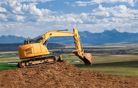 Big Yellow Bulldozer On A Heap Of Soil With Mountains In The Background