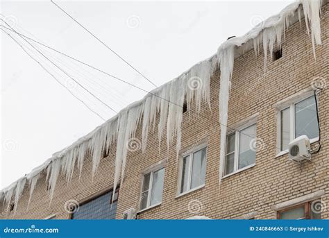 Big Icicles On The Roof Of A Townhouse On A Snowy Winter Day Among Thaw