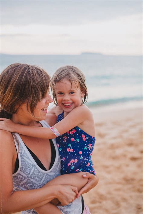 Young Mom Smiling And Holding Her Daughter On Tropical Beach At Sunset