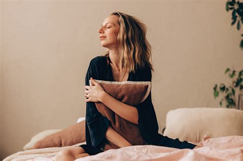 Beautiful Blonde Woman In Sleepwear Sitting On Her Bed Hugging A Pillow