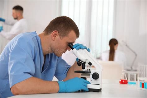 Scientist Using Microscope At Table And Colleagues Medical Research