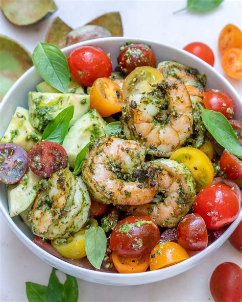 A White Bowl Filled With Shrimp Tomatoes And Pesto On Top Of Lettuce