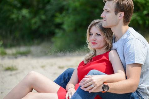 Young Couple Sitting On The Sand Smiling And Hugging Stock Image