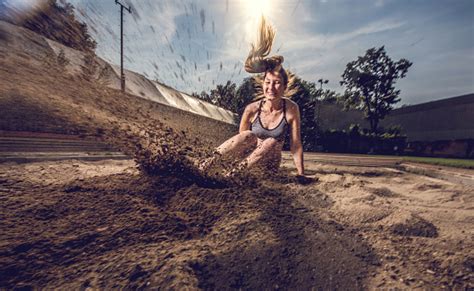 Young Female Athlete Landing In Sand After A Long Jump Stock Photo