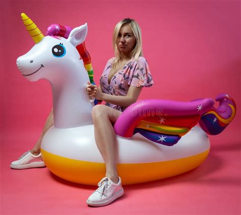 A Beautiful Blonde Girl In A Sundress With Slim Legs In White Sneakers Sits On An Inflatable