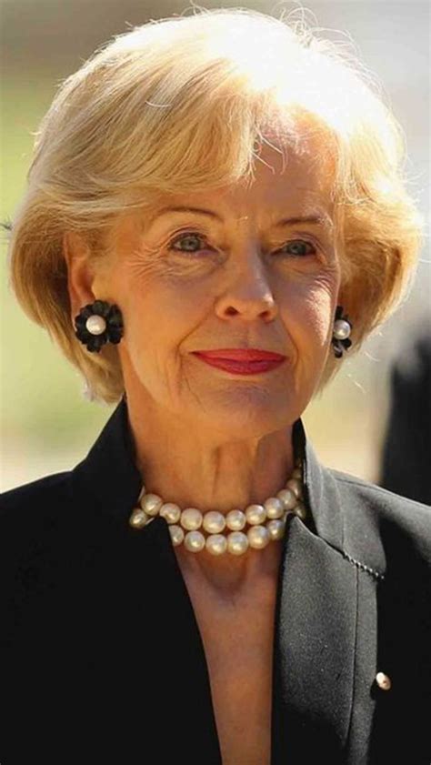 an older woman with blonde hair and pearls on her neck wearing a black suit smiling at the camera