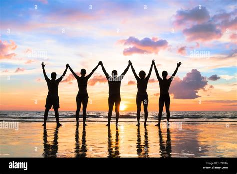 Silhouette Of A Group Of People Holding Hands Up On The Beach With A