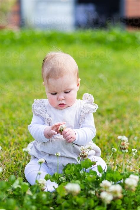 Image Of Happy Baby Sitting Outside On Grass In Backyard Picking Clover
