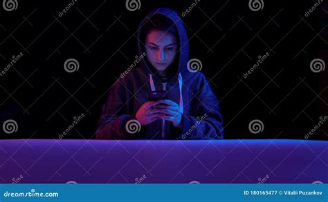 Young Woman In A Hood With A Smartphone Hacker Makes A Hack Through