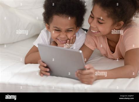 Cheerful Sister And Brother Lying On Bed Using Tablet Computer Stock