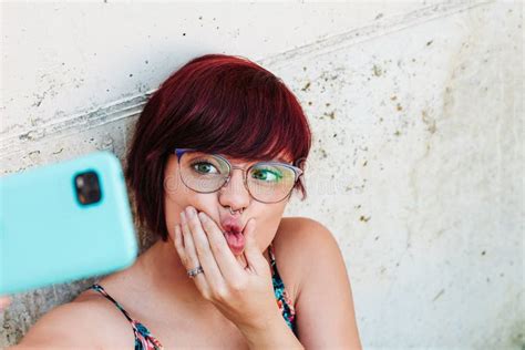 joven mujer con pendientes y perforaciones en la cara tomándose un selfie con su teléfono móvil