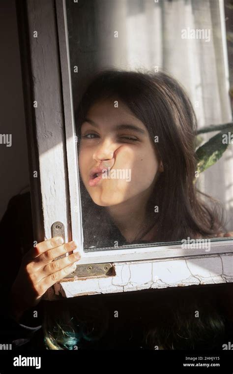 Funny Ethnic Girl Pressing Face Against Window And Looking At Camera Through Glass While Having