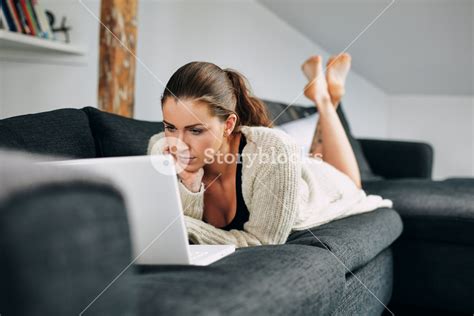 Portrait Of Beautiful Young Woman Working On Laptop While Lying On Sofa