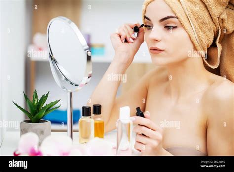 Pretty Woman In A Towel On Her Head Applies Makeup On Her Face At Home