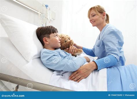 Happy Child Lying In Bed In Hospital Room Hugging A Teddy Bear Looking