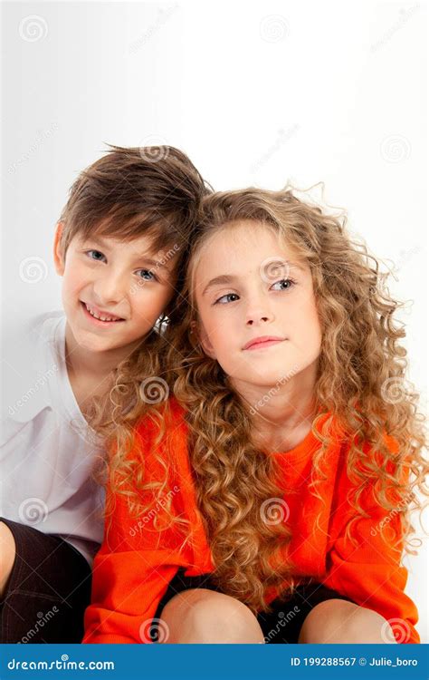 curly haired girl in an orange long sleeve t shirt sits next to her friend in a white t shirt