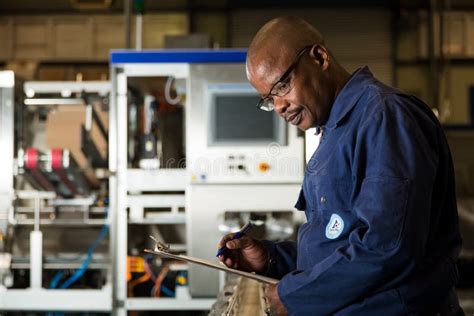 Black African Male Supervisor Checking A Clipboard On A Packaging Plant