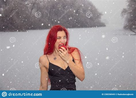 Redhead Woman Eating Apple Outside On Snowfall Winter Landscape Stock
